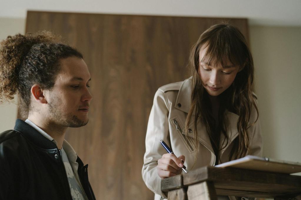 a woman signing a document beside a man