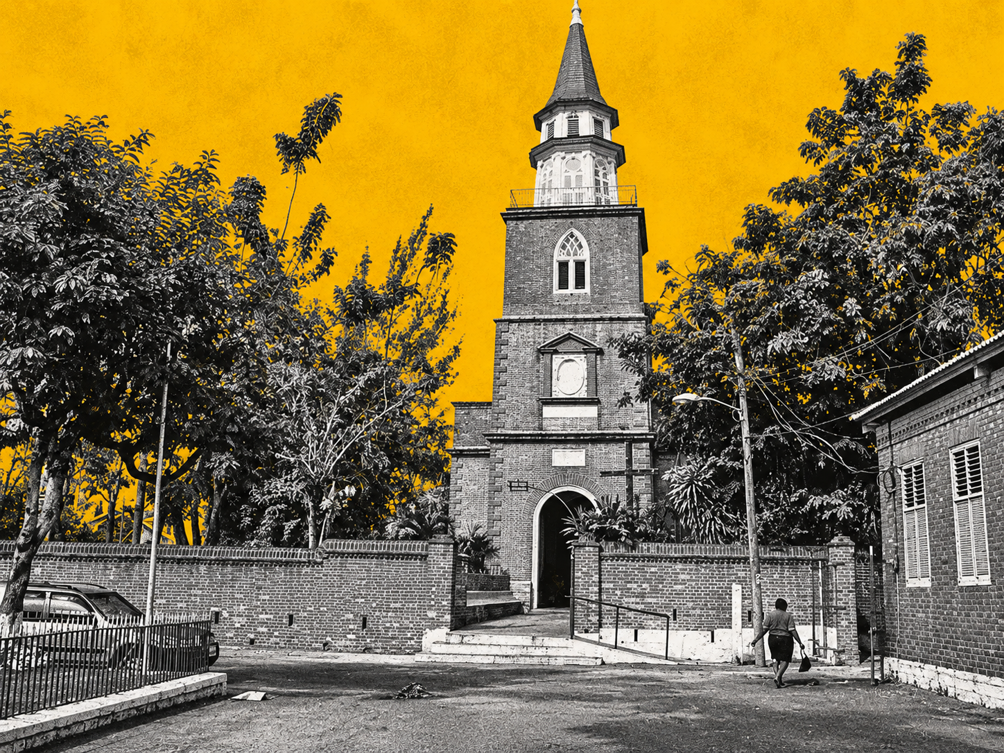 A historic Jamaican church stands behind its brick boundary wall, its tall steeple rising above mature trees and the surrounding community. Reworked in Jamaica Homes News’ distinctive yellow and greyscale editorial style, the image highlights the enduring presence of the church within Jamaica’s built landscape and social history.