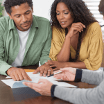 A couple reviews important documents with a professional adviser, highlighting the value of clear guidance, informed decisions and careful planning when navigating the property market.