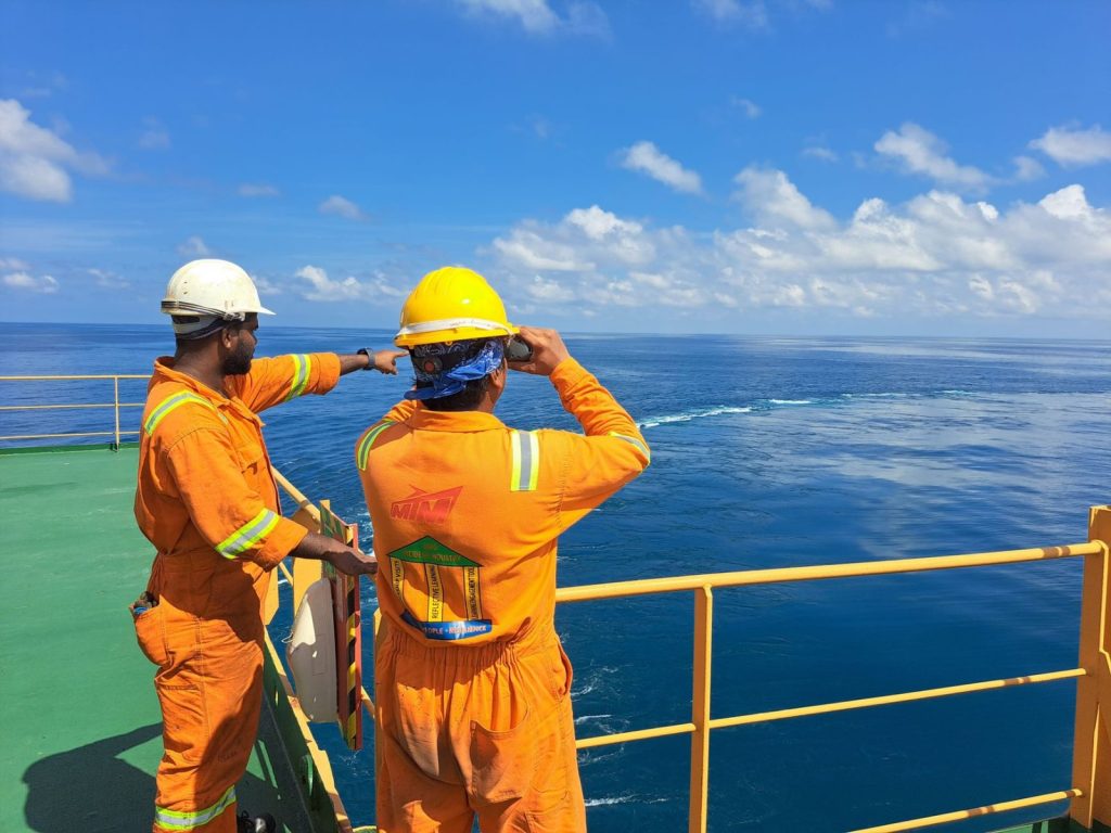 Oil Explorer Raises £500,000 as Jamaica Search Presses On two men in orange safety gear stand on the deck of a ship - Photo by Atmadeep Das