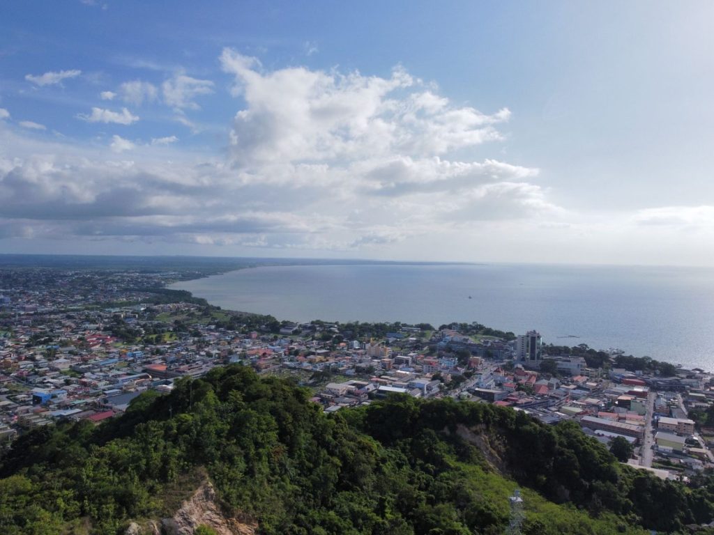 Guyana Races to Fill a 78,000-Home Gap aerial view of coastal city with blue sky and sea - Photo by Anderson Jagradatt