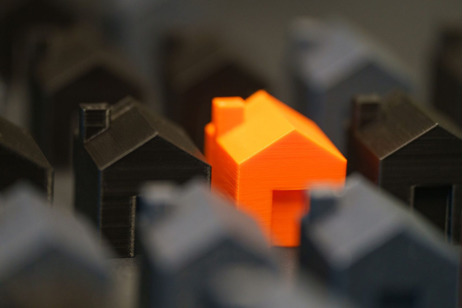 striking orange model house amidst black miniatures - Photo by Jakub Zerdzicki