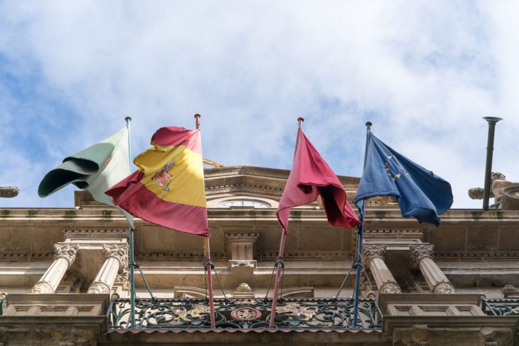 flags waving on old ornate city building on fine day - Photo by ArtHouse Studio