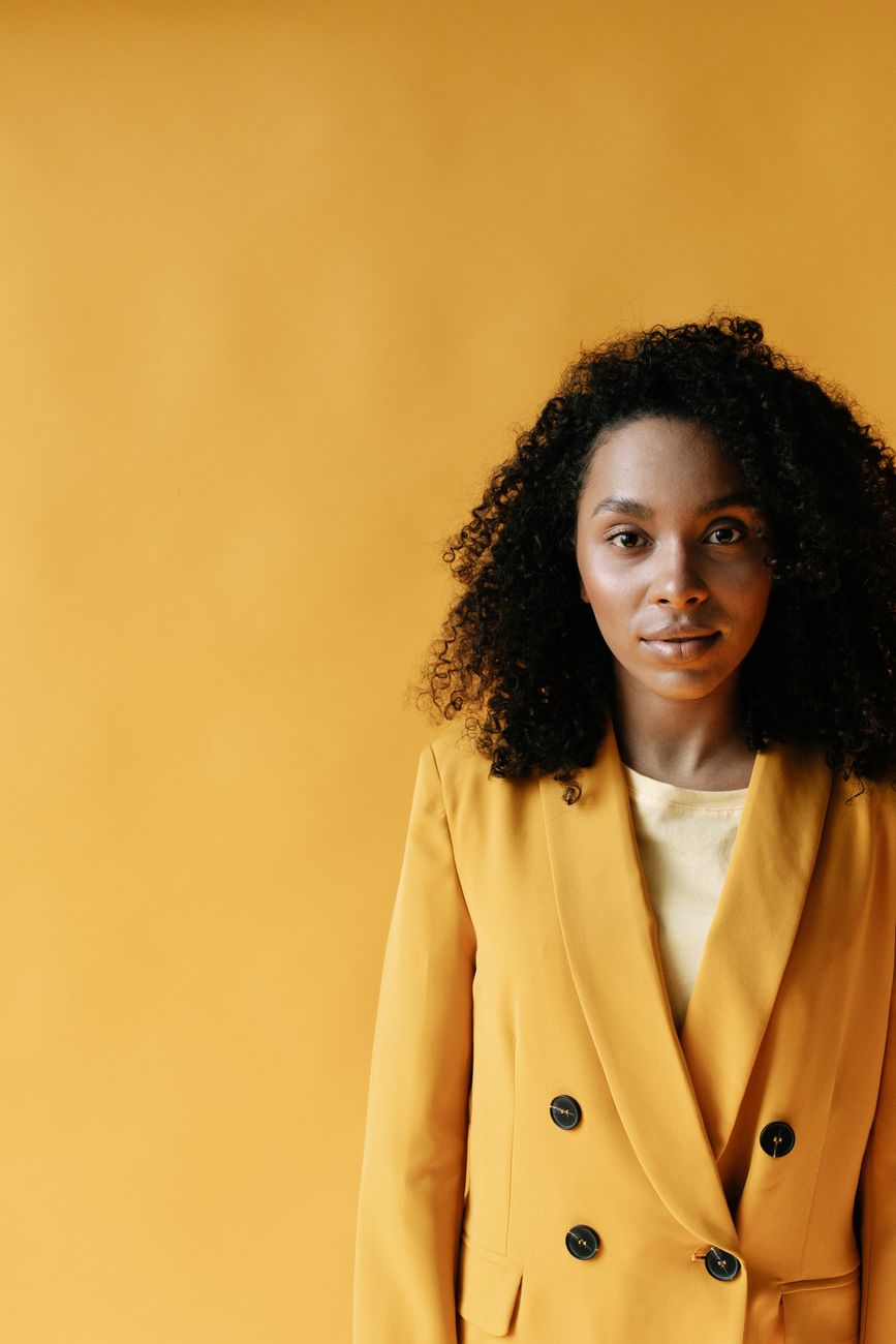 woman in yellow blazer standing beside yellow wall - Photo by Ivan S