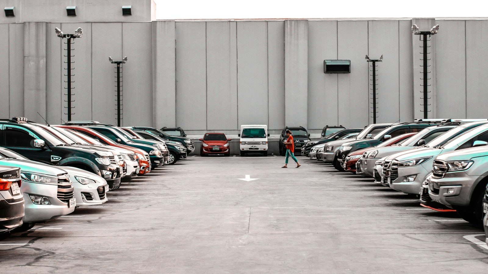 Rows of parked cars and SUVs lined up in a walled vehicle lot as a person walks between them