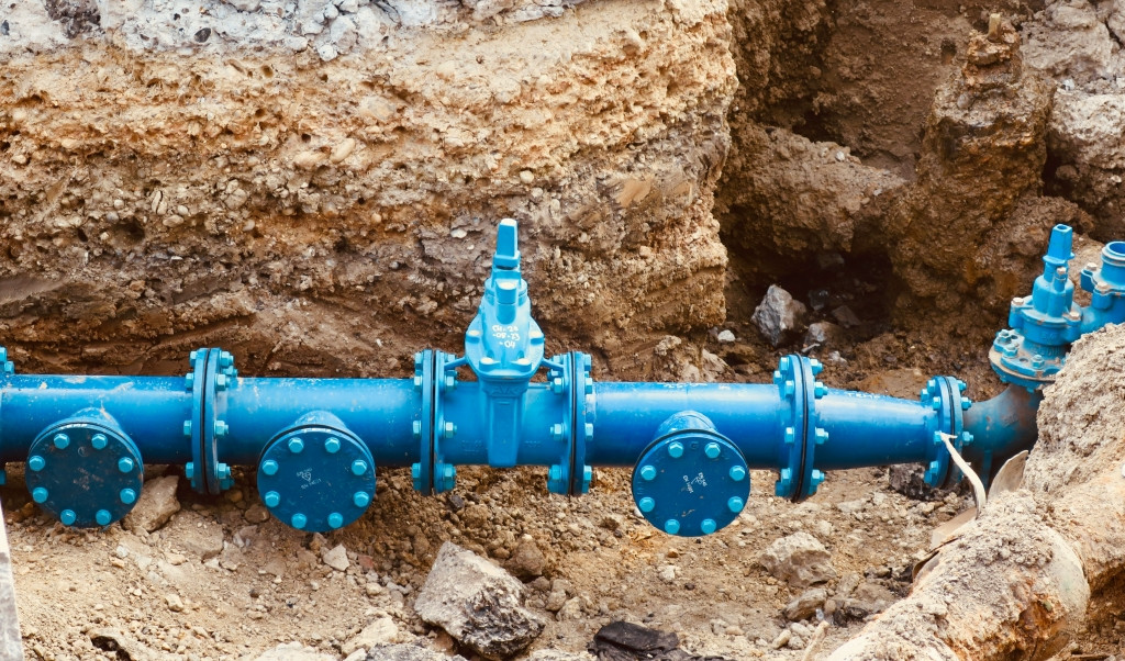 Real photograph of blue water supply pipes and valves in an excavated trench; generic image, not the Braco leak