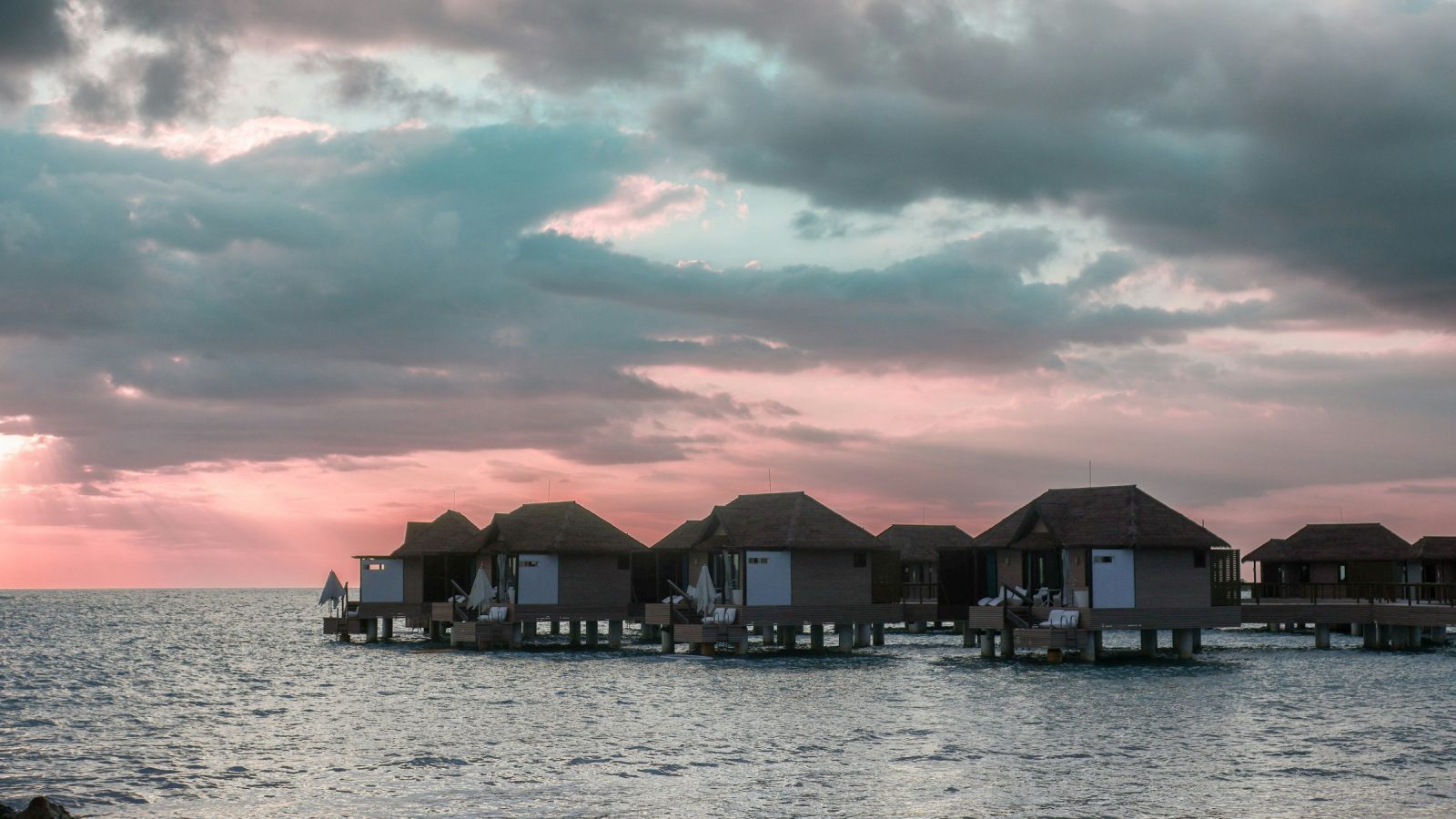Overwater guest suites on stilts at dusk under heavy cloud off the Westmoreland coast of Jamaica
